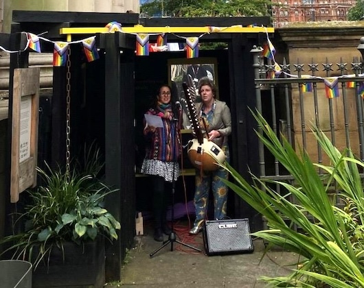 This image shows two people, playing music together under the shelter of the pocket park. They appear to be part of a street performance, with a guitar and other musical instruments visible.